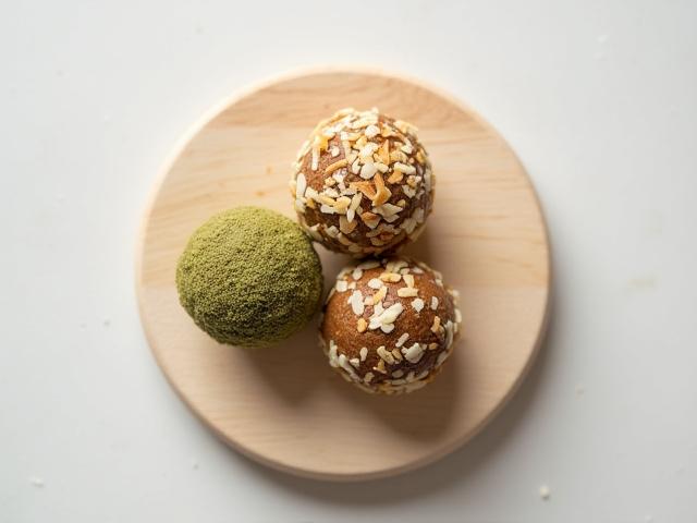 Small, round energy balls, coated in coconut flakes on a rustic wooden board